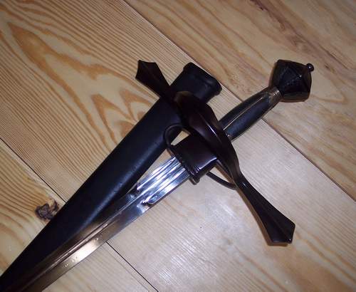 A medieval sword with a black hilt and scabbard on a wooden surface.