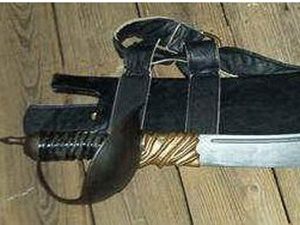 Sword with leather sheath on wooden floor.