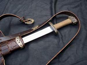 A traditional dagger with a leather sheath and strap on a dark fabric.