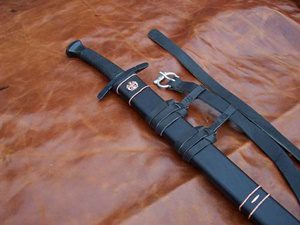 Black sword with sheath on leather surface.