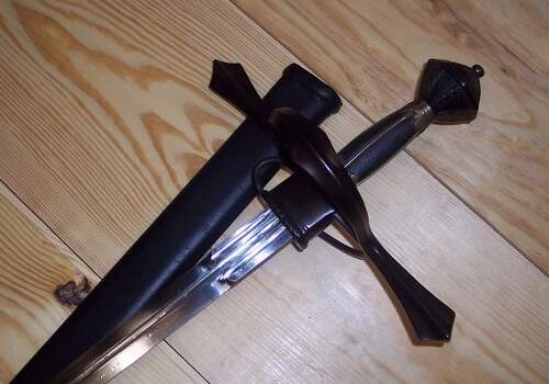 A medieval sword with a black hilt and scabbard on a wooden surface.